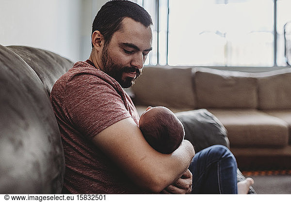 Dark-haired bearded father lovingly holding newborn