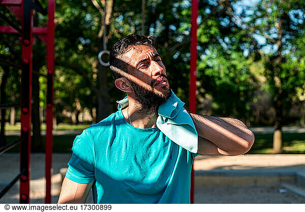 Dark-haired man with beard wiping his sweat after workout. Outdoor fitness concept.