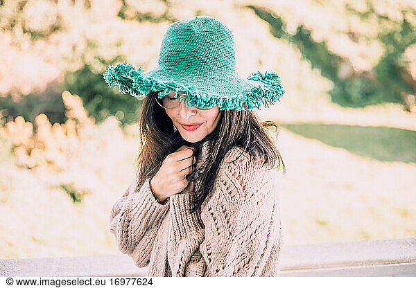Dark haired woman in green hat and glasses enjoying a sunny afternoon