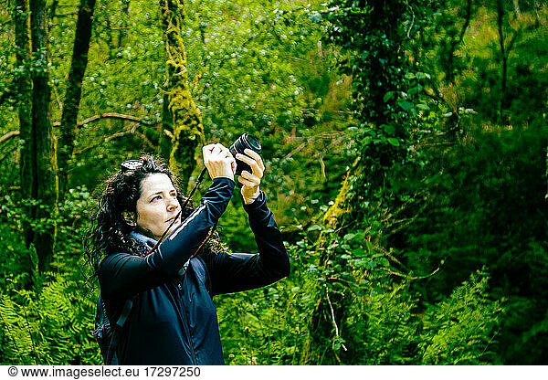 Dark-haired woman taking photos in the forest