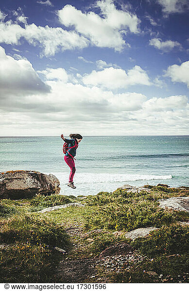 Dark-haired woman with red backpack  jumping from a rock near the sea