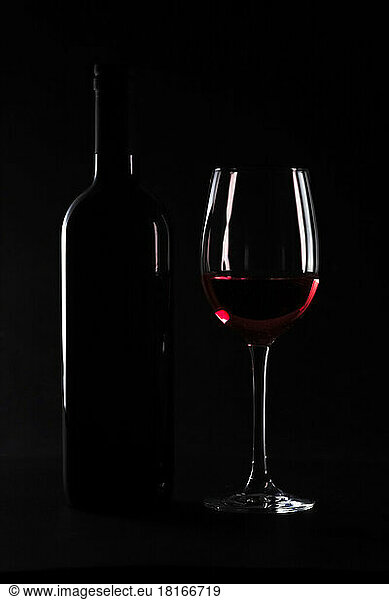 Dark studio shot of bottle and glass of red wine