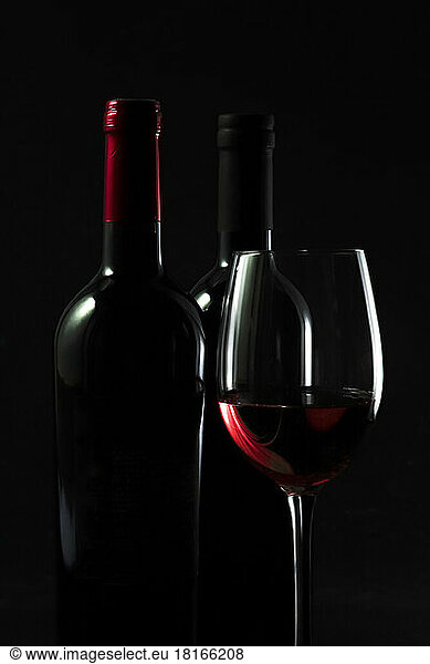 Dark studio shot of bottles and glass of red wine