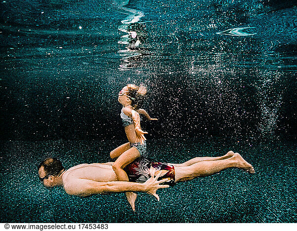 daughter and father swimming together in a pool during summer
