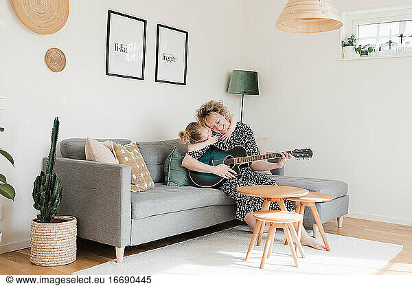 daughter giving mother a hug whilst she plays guitar at home