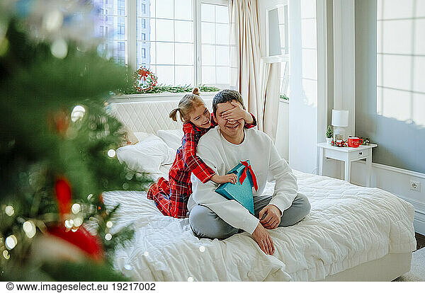 Daughter giving present and covering father's eyes on bed at home