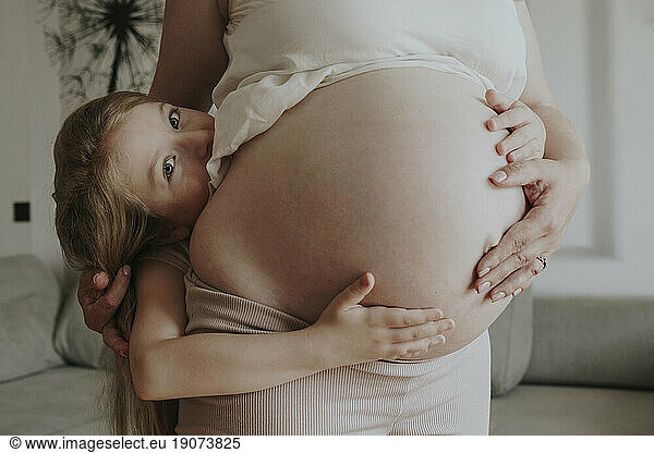 Daughter hugging pregnant mother at home