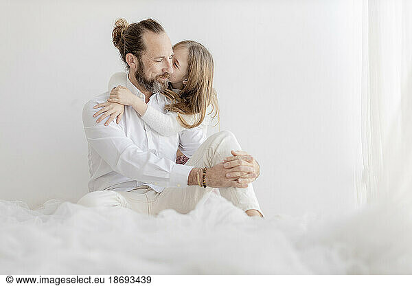 Daughter kissing father sitting in front of wall