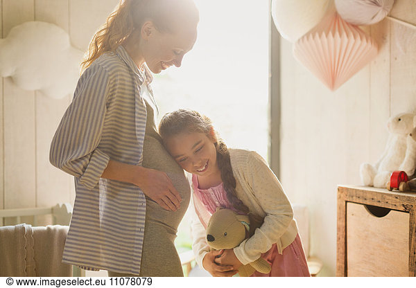 Daughter listening to pregnant motherís stomach in nursery