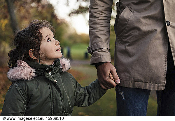Daughter looking at father while holding hands in park during autumn
