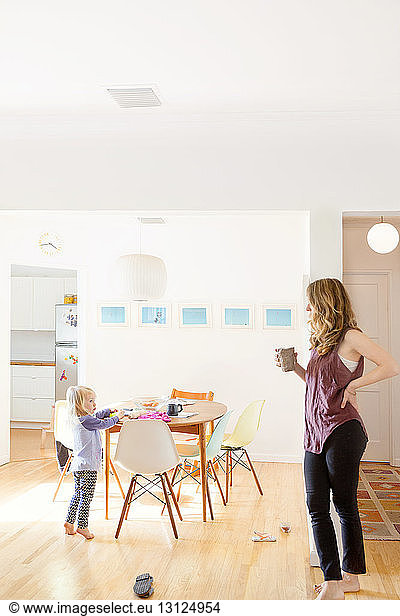 Daughter looking at mother holding coffee cup at home