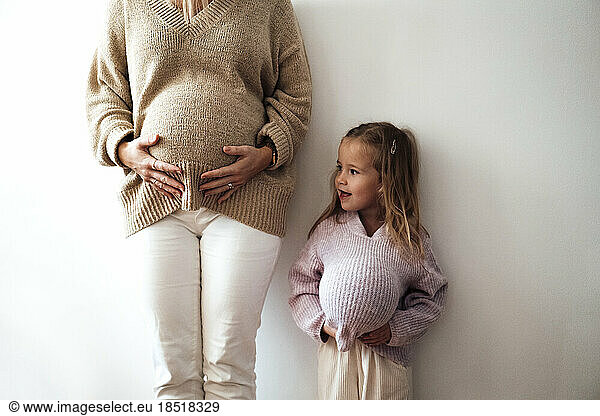 Daughter mimicking mother's pregnancy in front of wall