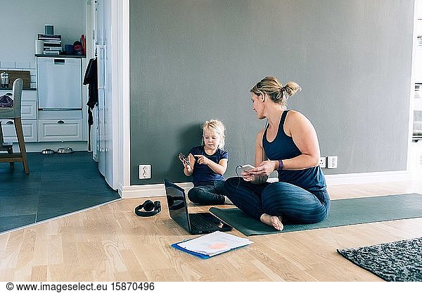 Daughter pointing at smart phone to mother while sitting on exercise mat at home