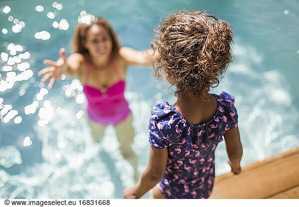 Daughter preparing to jump into arms of mother in sunny swimming pool