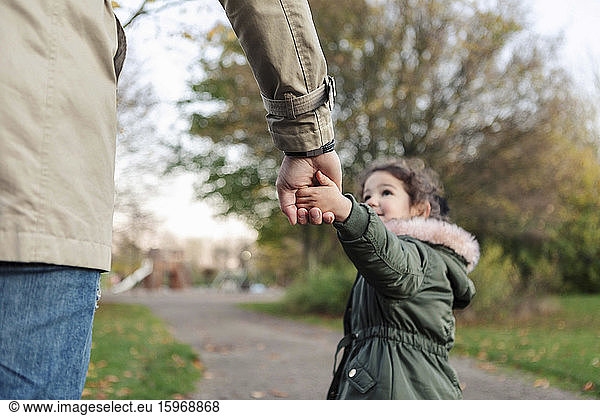 Daughter pulling father while holding hands in park during autumn