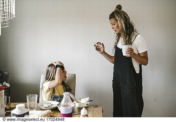 Daughter refusing to eat breakfast while mother standing by with coffee cup at home