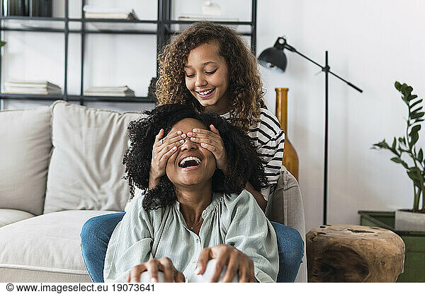 Daughter sitting on couch surprising mother covering her eyes