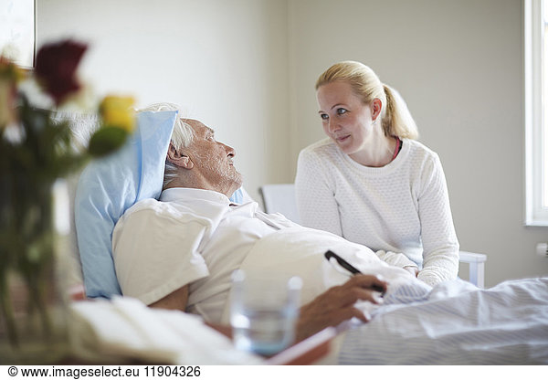 Daughter talking to senior man reclining on hospital bed