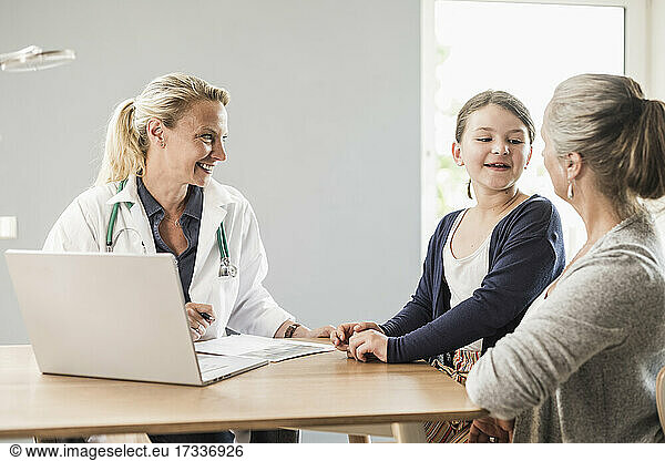 Daughter talking with mother while sitting by doctor at office