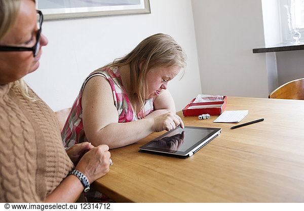 Daughter with down syndrome using digital tablet  mother looking