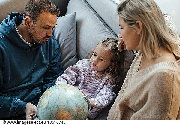 Daughter with parents looking at globe on sofa at home