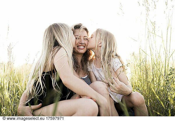 Daughters kissing mother at field in summer