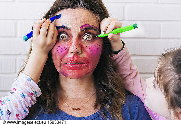 Daughters painting coloful make up on mother's face