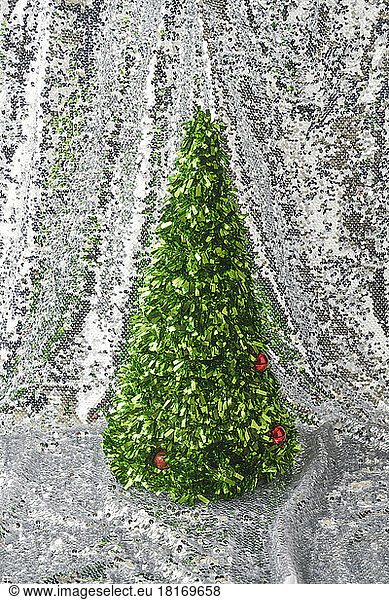 Decorated confetti Christmas tree against shiny silver sequins