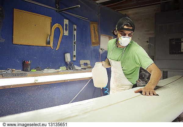 Dedicated male worker working on surfboard in workshop
