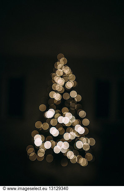 Defocused image of illuminated Christmas tree in darkroom at home