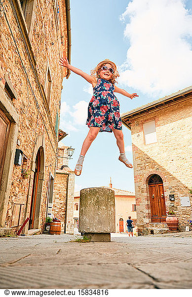 Delighted child jumping up on sidewalk in town in Tuscany