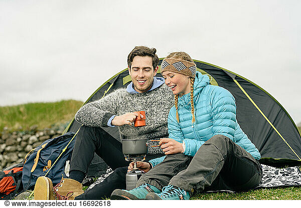 Delighted couple brewing beverage near tent
