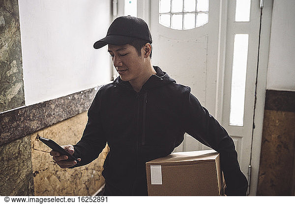 Delivery man using mobile phone while holding package against door