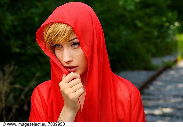Demure young attractive blond woman with red veil on railroad tracks