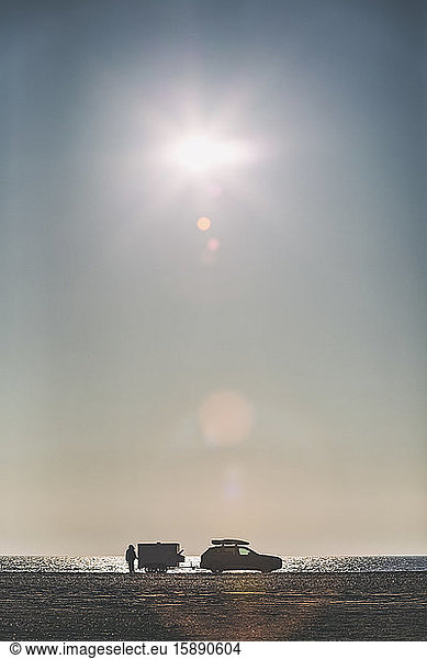 Denmark  Romo  Sun shining over person standing beside car parked on coastal beach
