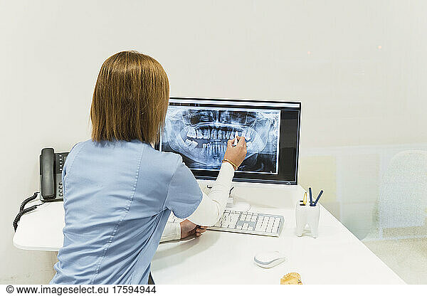 Dentist examining teeth X-rays over intraoral scanner screen at desk