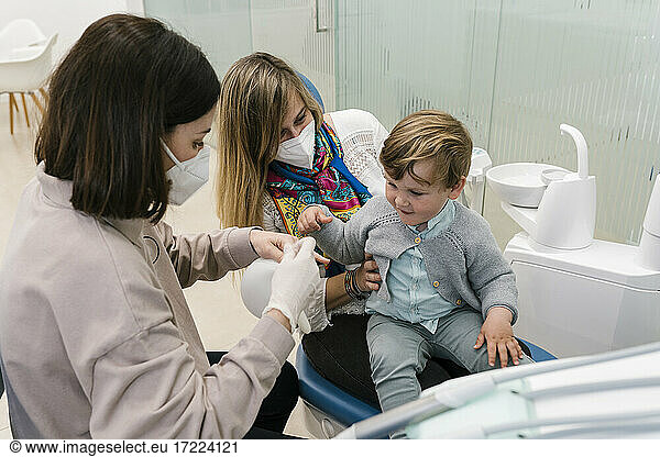 Dentist wearing protective face mask sitting by woman and boy in clinic
