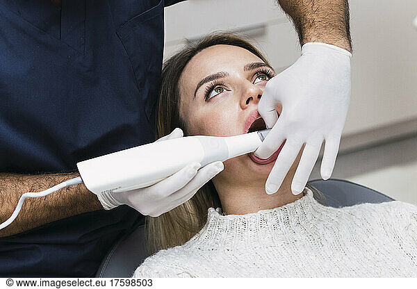 Dentist with intraoral scanner examining patient's teeth at clinic