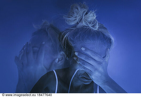 Depressed woman with head in hands against blue background