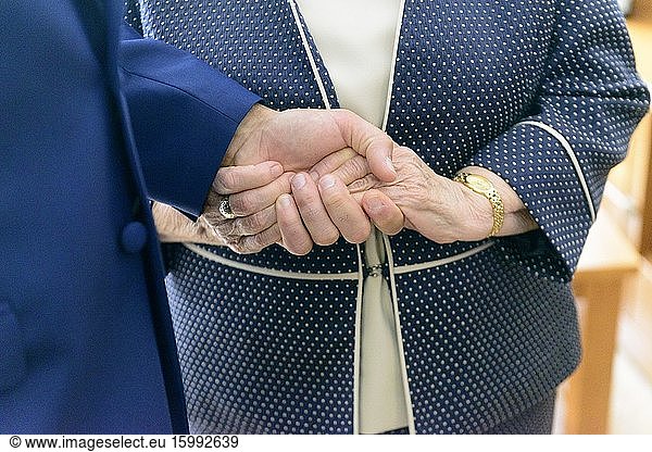 Der Bräutigam hält am Tag der Hochzeit liebevoll die Hände seiner Großmutter