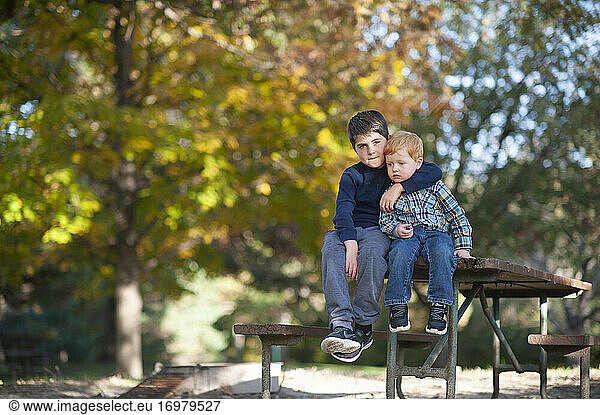 Der große Bruder legt seinen Arm um den kleinen Bruder  der auf dem Picknicktisch sitzt