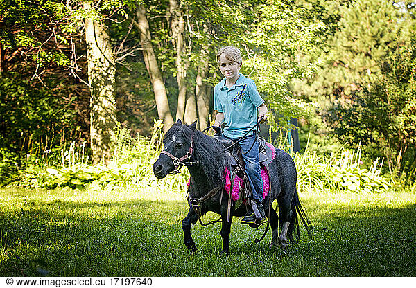 Der kleine Blonde reitet auf seinem kleinen schwarzen Pony durch die Landschaft.