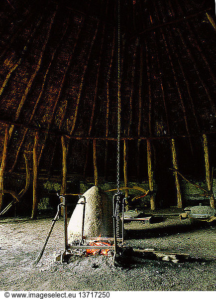 Der Versuchsbauernhof Little Butser in Hampshire  das Innere einer exakten Nachbildung einer Behausung aus der Eisenzeit. Das Gerüst des Hauses besteht aus Baumstämmen  das Dach ist strohgedeckt und die Wände sind aus Lehm und Flechtwerk gefertigt. Blick in das Innere der Hütte und auf die offene Feuerstelle. Britannien. Keltisch. Eisenzeit.