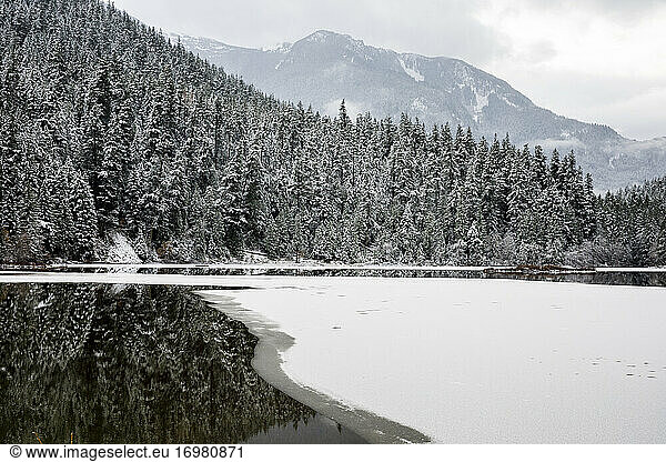 Der von Bergen und schneebedeckten Wäldern umgebene See beginnt zu gefrieren
