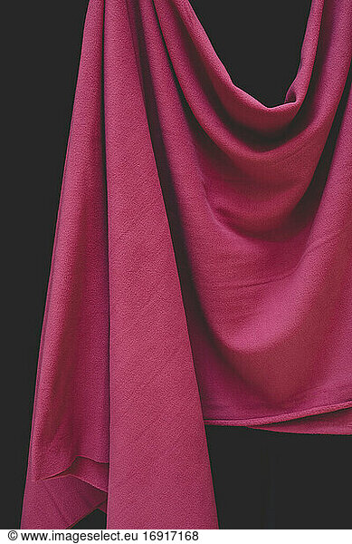 Detail of hanging pink fabric against black background