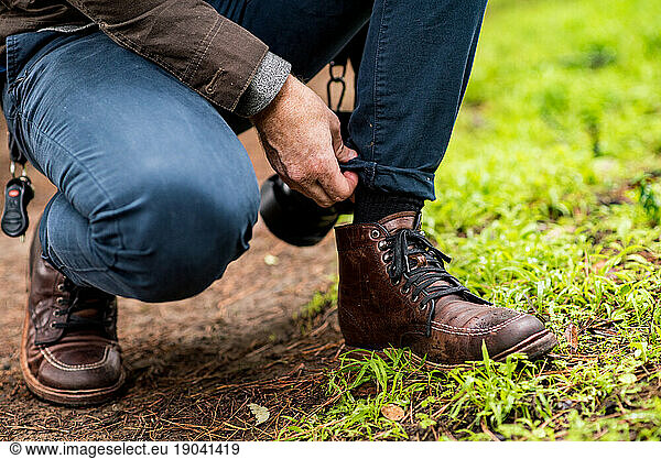 Detail of man adjusting pant leg with focus on leather hiking boots