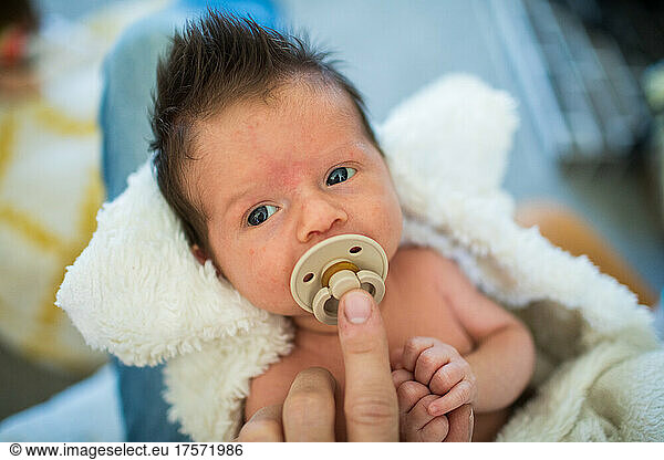 Detail of parent holding pacifier in newborn baby's mouth.