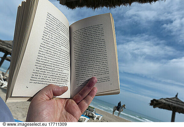 Detail Of Someone Reading A Paperback Book On A Sun Lounger On The Beach; Djerba  Tunisia