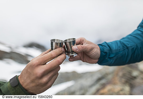 detail of two men toasting shot glasses in the mountains.