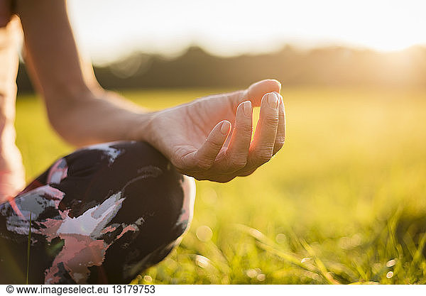 Detail of woman in lotus position on rural meadow at sunset